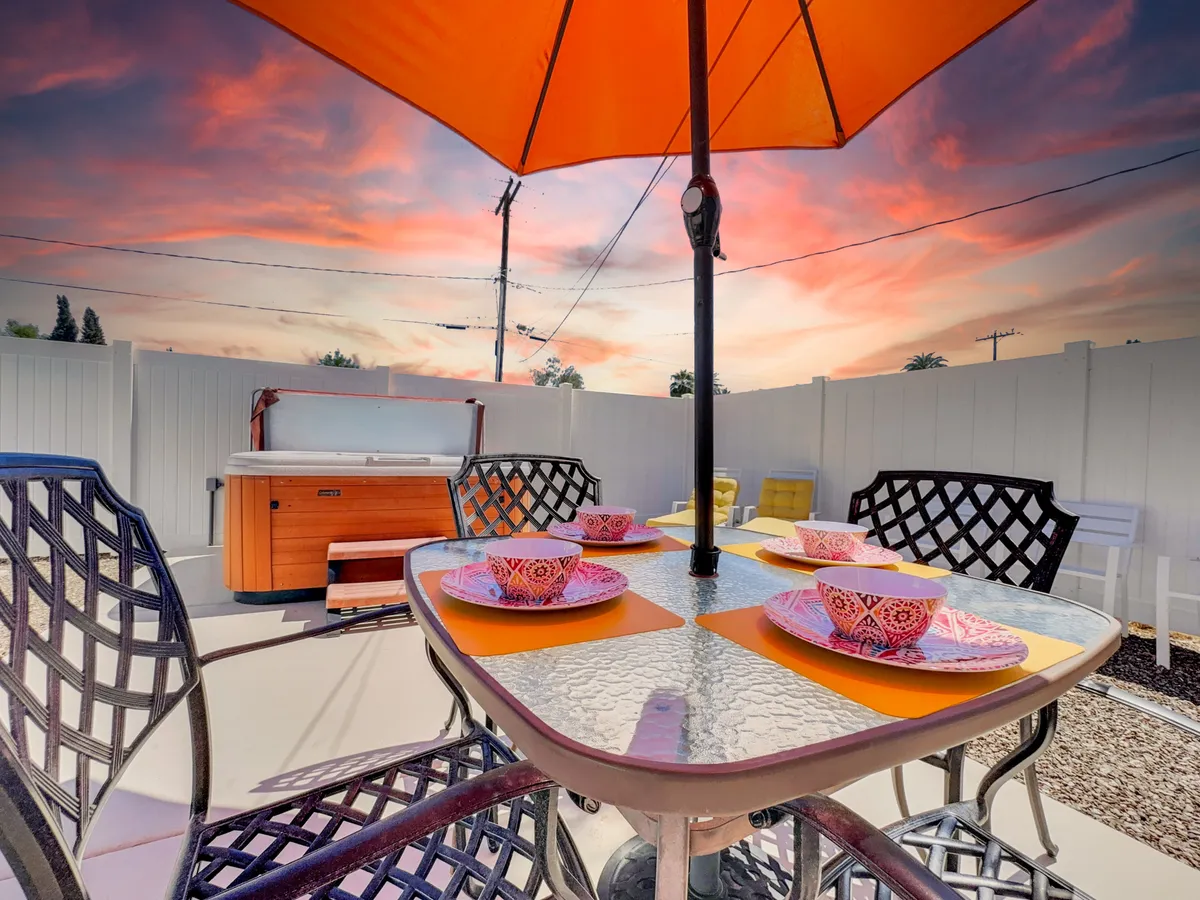 The image features a cheerful outdoor dining space under an orange umbrella, with decorative plates and a hot tub nearby. The atmosphere is lively, relaxed, and ideal for socializing or unwinding, suggesting a seamless transition between fun outings and comfortable evenings at home.