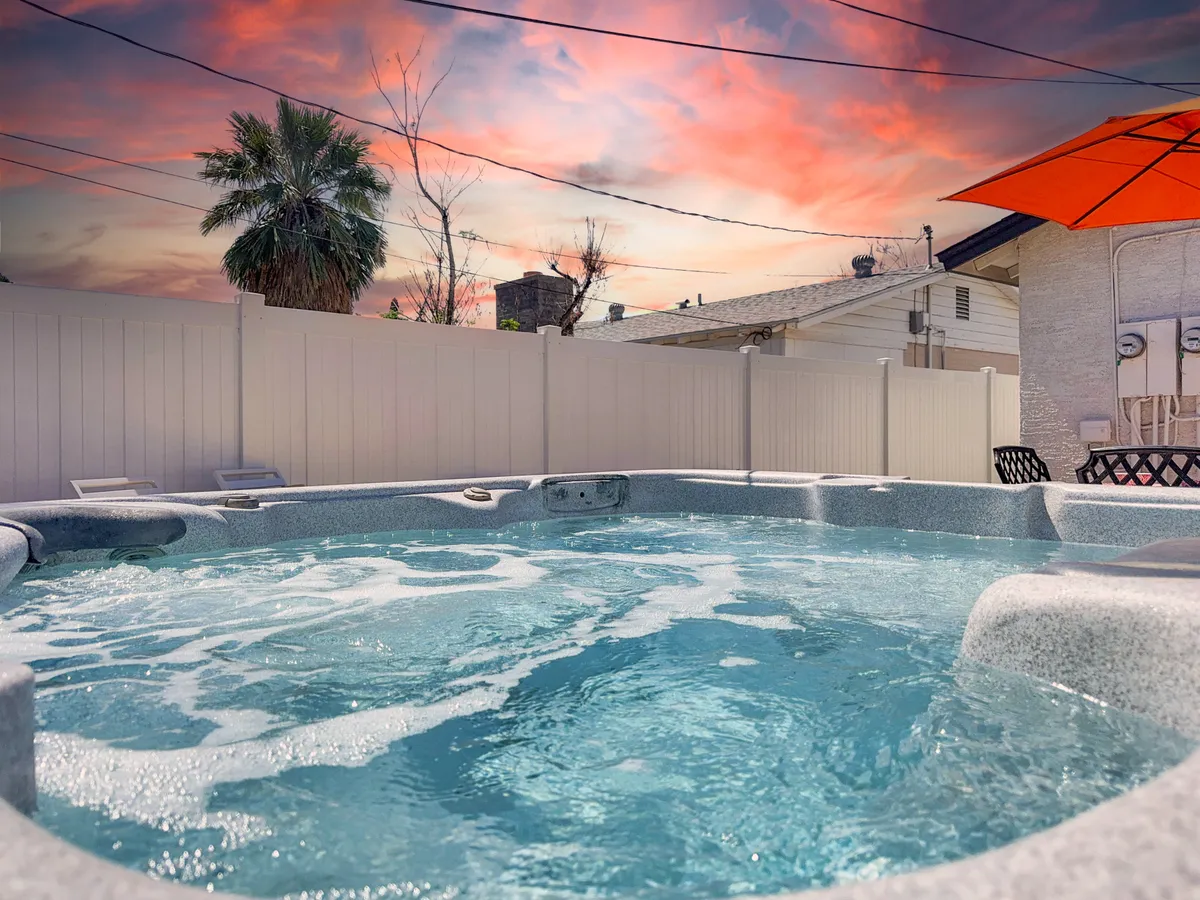 This exterior image features a private hot tub set on a patio, framed by a vibrant orange umbrella and illuminated by a dramatic sunset sky. The tranquil atmosphere highlights a space perfect for relaxation and connection, with the warm glow of dusk enhancing the romantic appeal.
