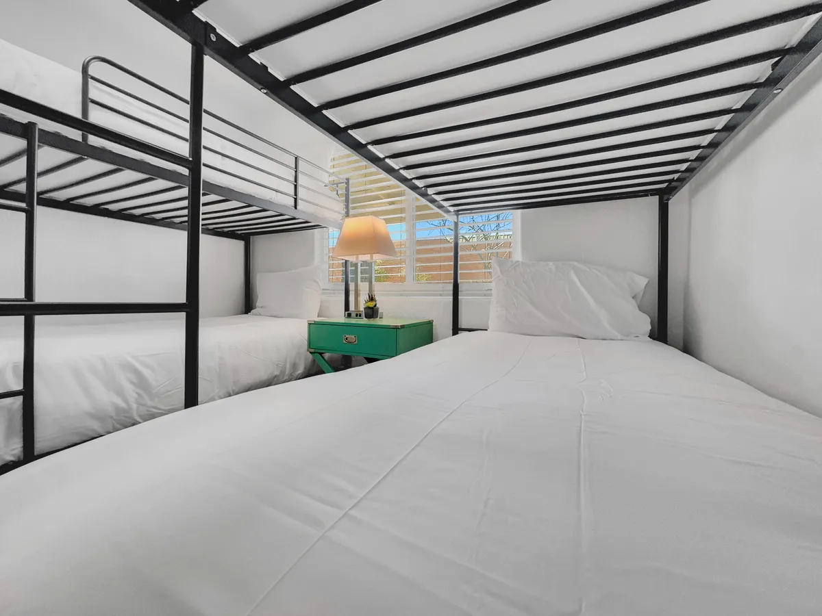 A cheerful bedroom with a set of bunk beds, a table lamp, and a green bedside table. The space is designed for sharing, offering a welcoming atmosphere ideal for families, friends, or colleagues. Soft lighting encourages bedtime stories or gentle wind-downs.