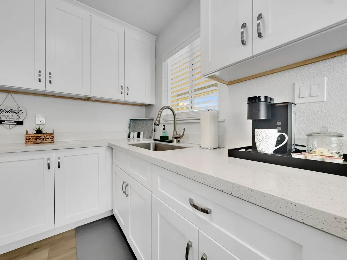 A stylish, inviting kitchen scene with a sleek coffee machine, white cabinets, a modern sink, and decorative touches like a woven basket. The layout suggests a space for both morning routines and relaxed gatherings.