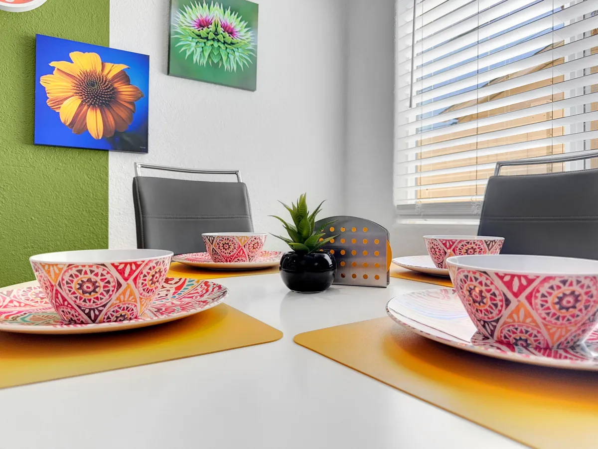 A vibrant dining area adorned with colorful plates, bowls, and lively wall art, with a small decorative plant enhancing the cozy, friendly vibe. The space is ideal for sharing casual meals or brunch before heading downtown.