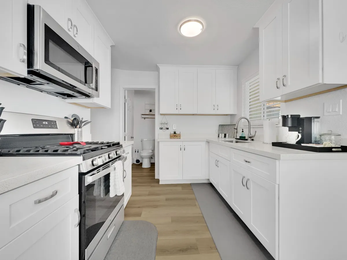 A bright, functional kitchen area featuring white cabinetry, a kitchen island with a sink, and stainless steel appliances. The space is arranged for both cooking and gathering, inviting family and friends to share in meal prep or conversation.