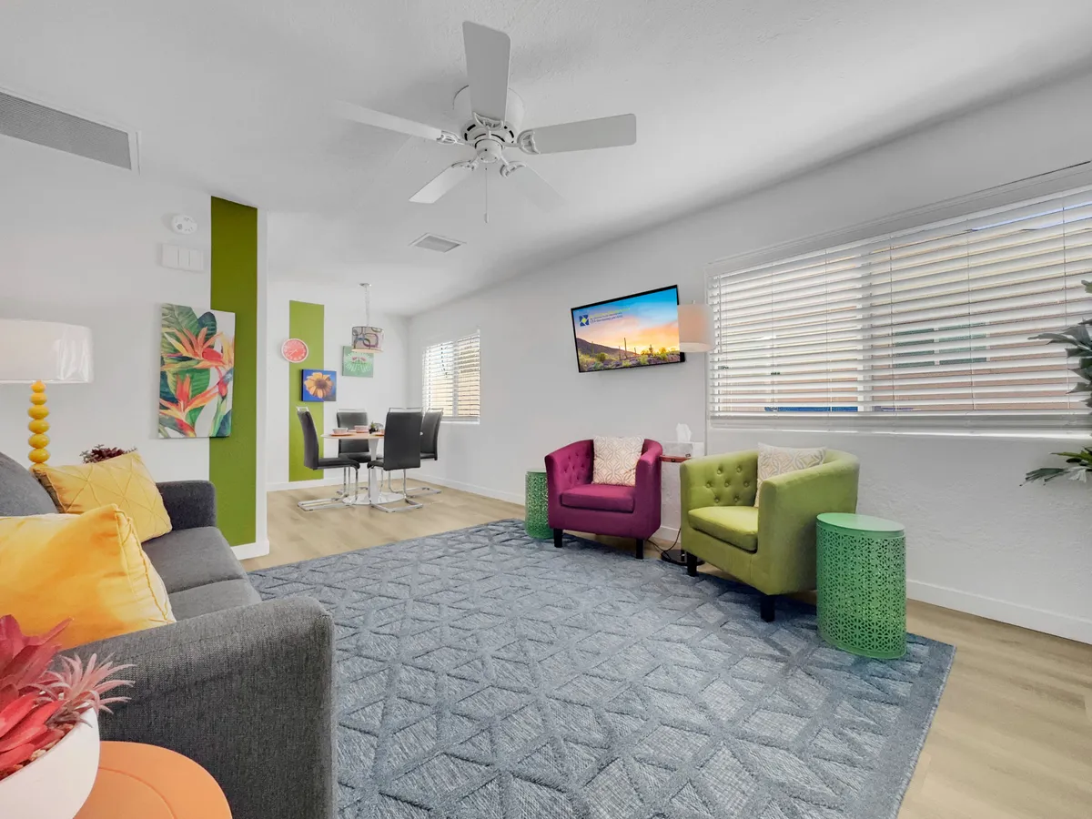 A cheerful living and dining area with colorful armchairs, a dining table positioned for easy access, vibrant decorative wall art, and a cozy patterned rug. The room exudes warmth and energy, emphasizing a welcoming atmosphere perfect for group gatherings.