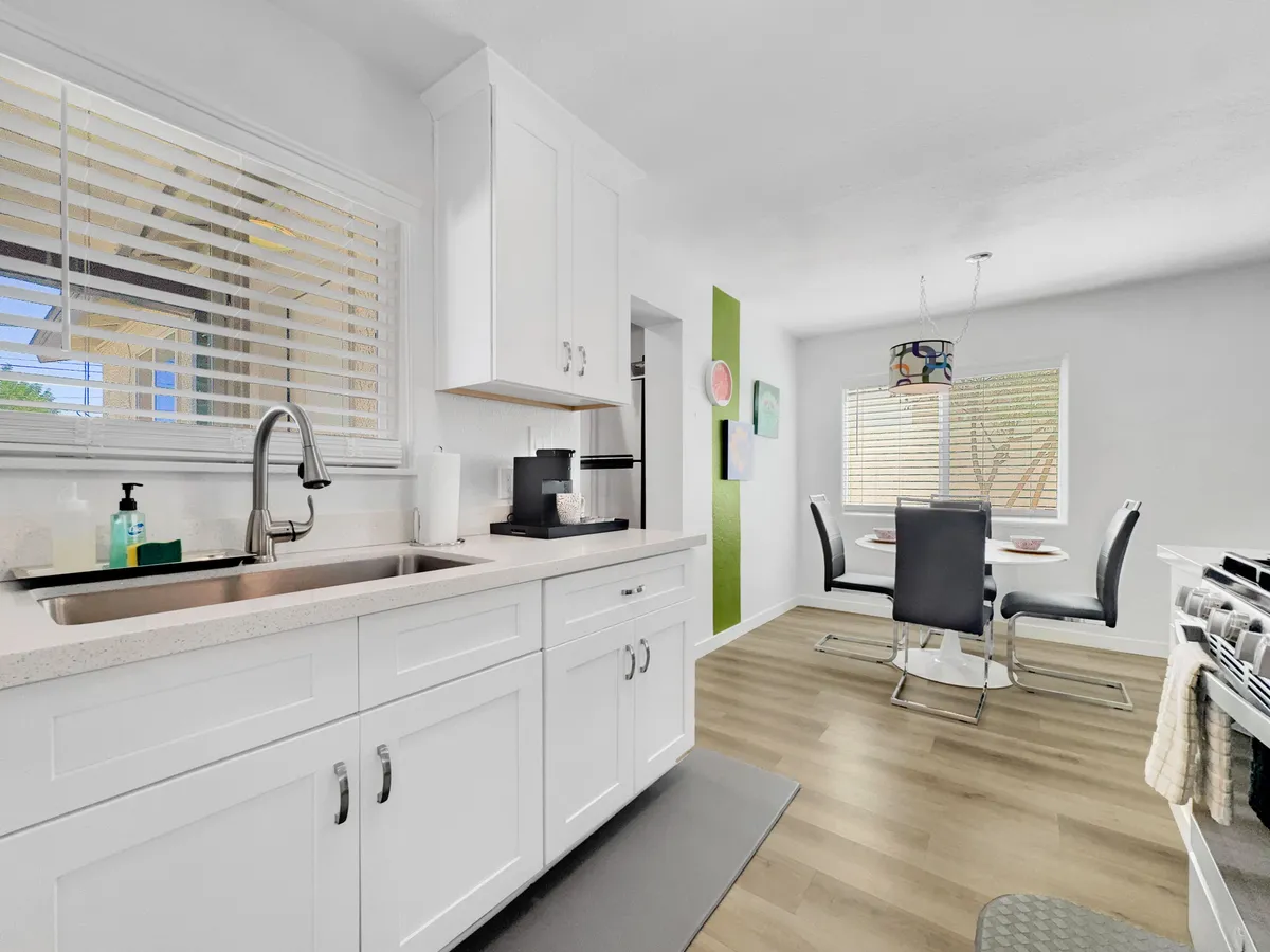 A warm, sociable kitchen and dining area, featuring a kitchen sink, dining table, and vibrant wall art. The space is set up for sharing meals and conversation, with a casual, inviting atmosphere.
