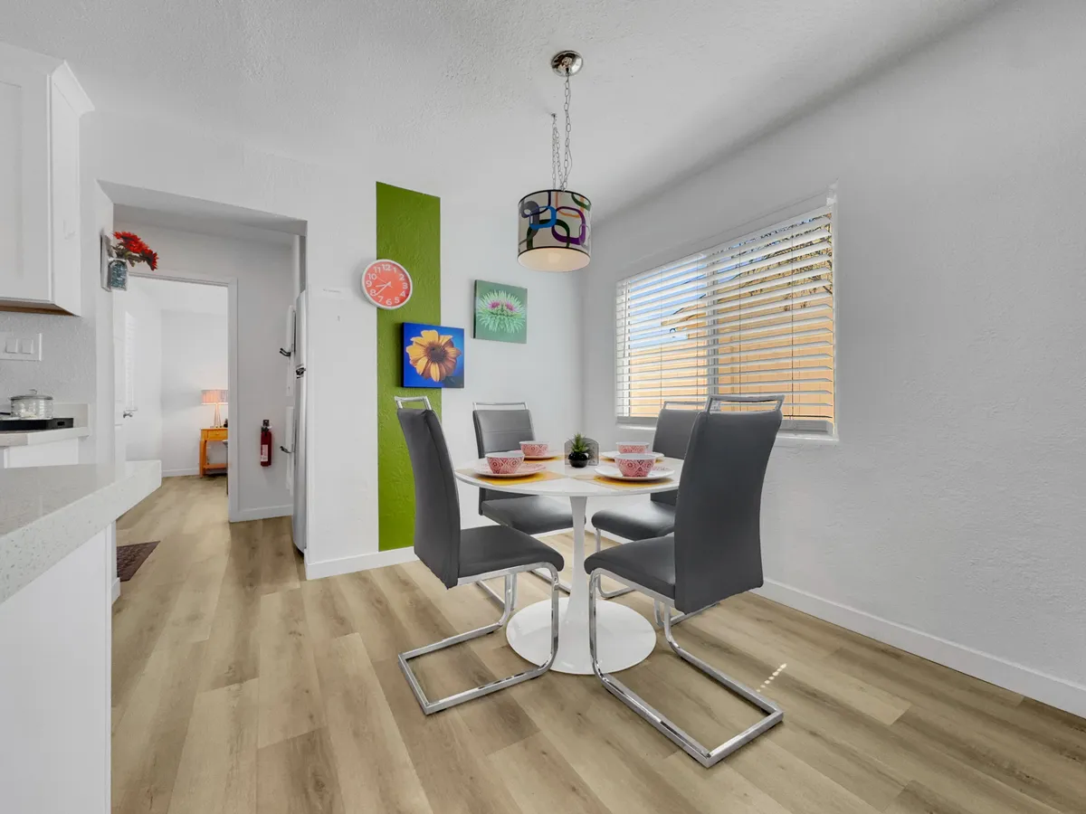 A round dining table set beneath a pendant light, surrounded by colorful wall art and bathed in natural light. The setup encourages shared meals and intimate gatherings, making it ideal for both family and friends.