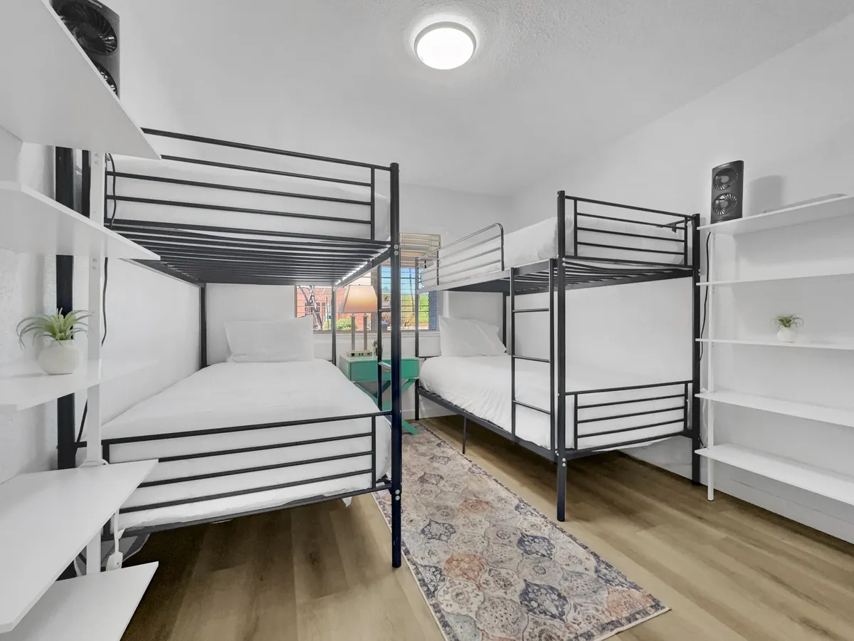 A comfortable bedroom setup with bunk beds and a cozy rug, evoking memories of late-night chats and shared experiences. Shelves and a relaxed atmosphere make this an ideal resting spot for the group after a day of exploration.