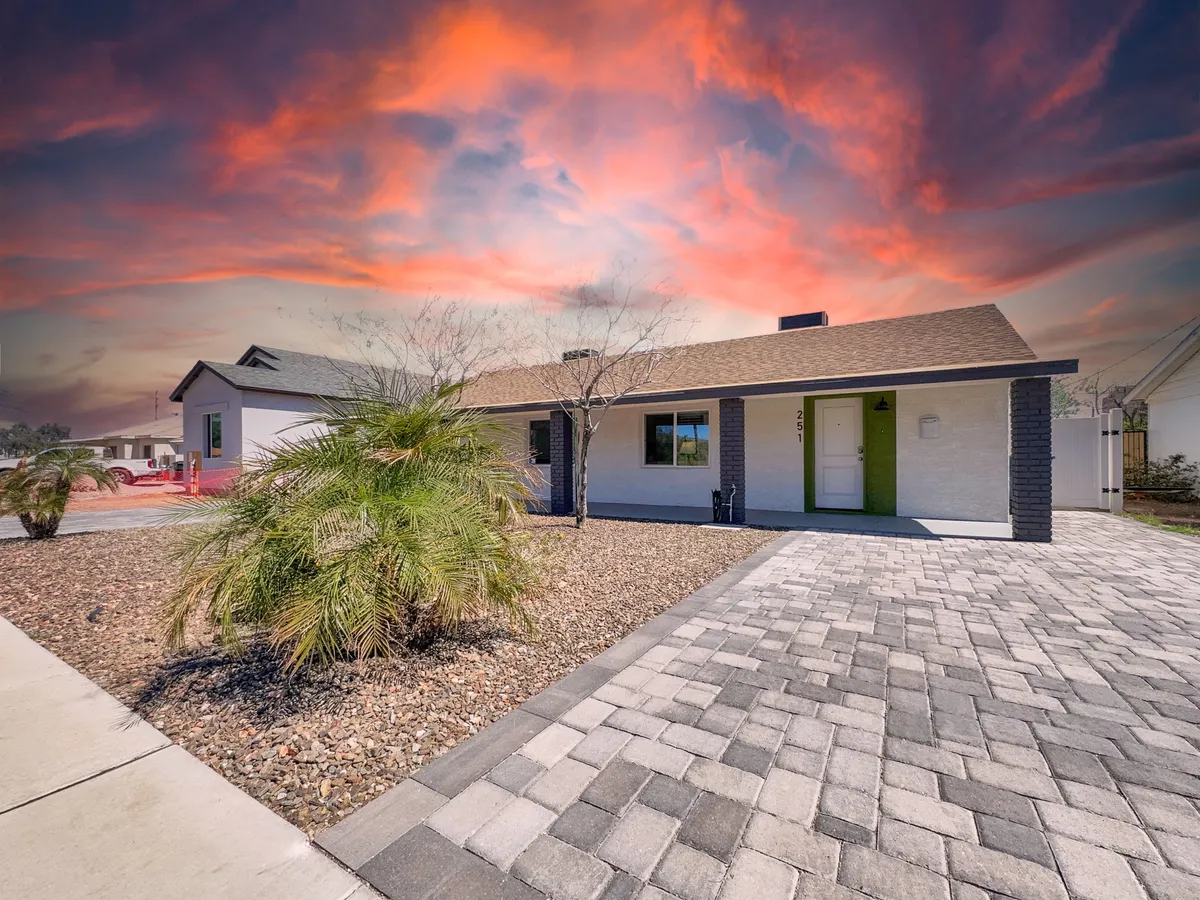 This image captures the vibrant exterior of the home, with a green front door, textured pavers, palm plants, and a vivid sky. The scene feels warm and inviting, and hints at the welcoming nature of the property and its connection to the outdoors.